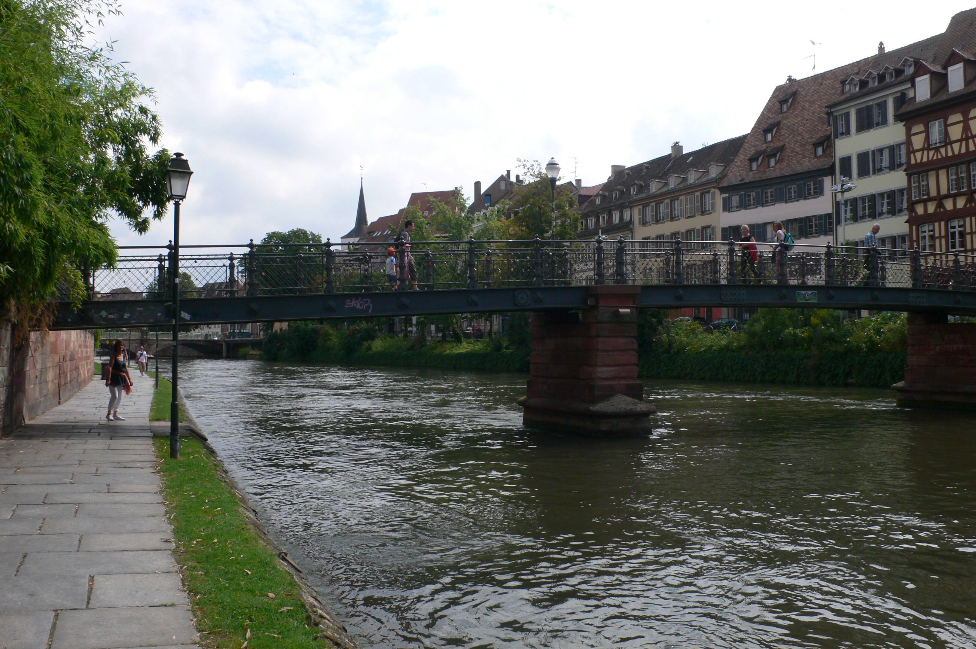 A pedestrian bridge over a river with buildings on either side.