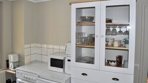 A kitchen with a microwave, coffee maker, and a cabinet with glassware and dishes. - Cottage in a quiet and green ski trails near hiking (Maisonsgoutte)