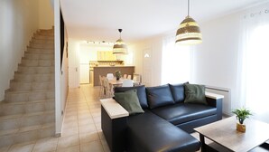 A modern living room with a black leather sofa, a wooden coffee table, and a staircase leading to a kitchen area. - Gîte de la truffière "Les Chênes  (Montagnac-Montpezat)