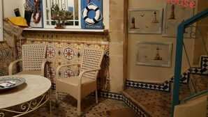 A cozy entrance with a wicker chair, a small table, and a decorative wall with nautical-themed artwork. - Lotus-Essaouira .com SEA VIEW - PRIVATE TERRACE - near BEACH (ESSAOUIRA)