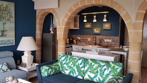 A living room with a sofa, a lamp, and a dining area with a kitchen in the background. - Lotus-Essaouira .com SEA VIEW - PRIVATE TERRACE - near BEACH (ESSAOUIRA)