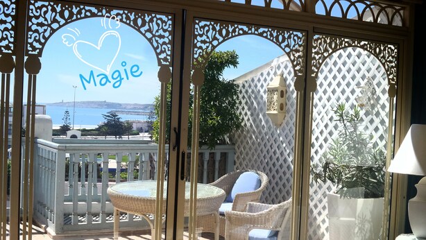 A balcony with wicker furniture, a view of the sea, and a decorative sign with the name "Magie". - Lotus-Essaouira .com SEA VIEW - PRIVATE TERRACE - near BEACH (ESSAOUIRA)