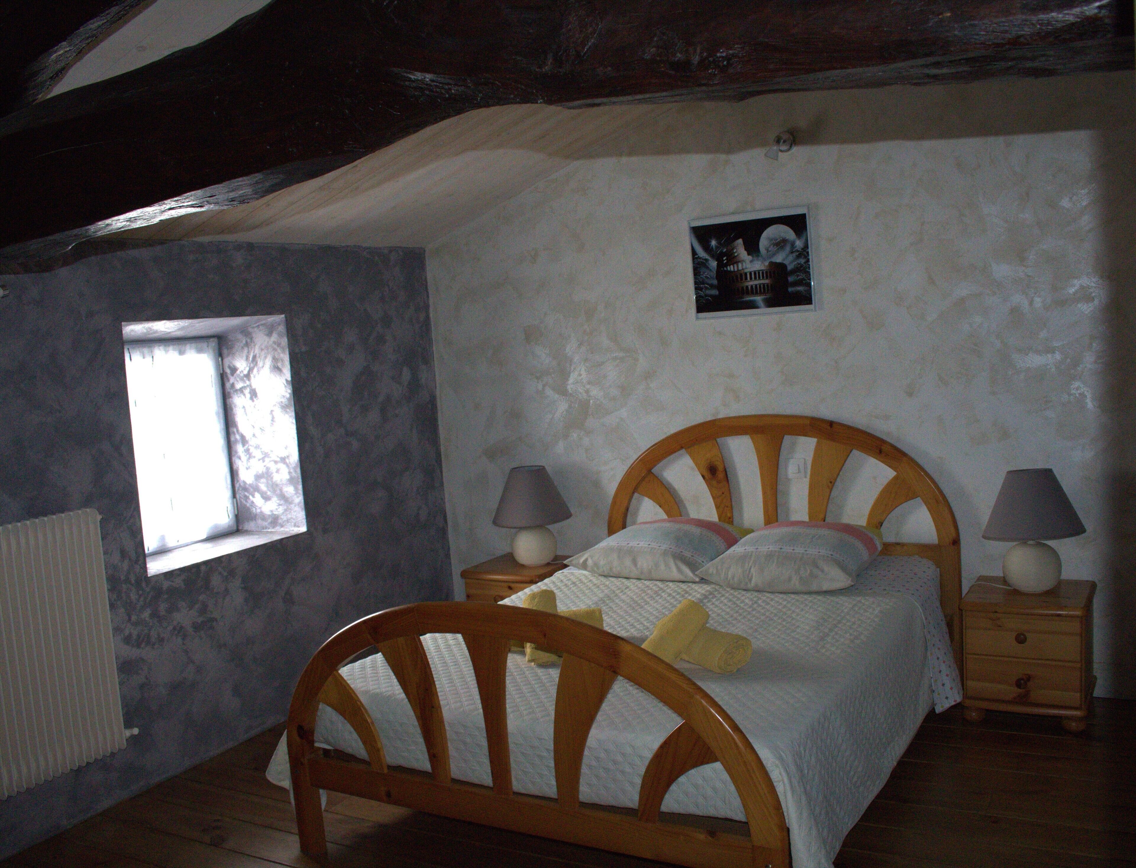 Une chambre à coucher avec un lit en bois, deux tables de chevet avec des lampes, une fenêtre et un tableau accroché au mur.