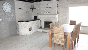 A rustic kitchen with a stone wall, a white clock, and a fireplace.