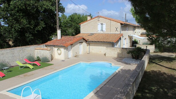 A rectangular swimming pool with a tiled deck, surrounded by a low stone wall.