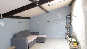 A cozy attic room with a grey sectional sofa, a small round table, and a shelf with potted plants.