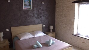 A bedroom with a large bed, two bedside tables, a night lamp, a painting on the wall, and a window with a view.