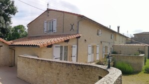 A two-story building with a tiled roof, stone walls, and multiple windows with shutters.