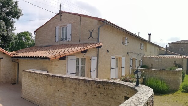 Un edificio de dos plantas con techo de tejas, paredes de piedra y varias ventanas con contraventanas.