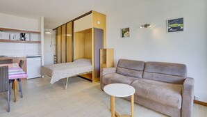 A compact living space with a kitchenette, a sofa, a small round table, and a bed with a wooden headboard. - HOSSEGOR Océan, studio for 3 people (HOSSEGOR)