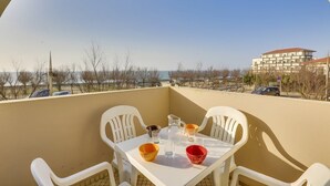 A balcony with a table set for two, chairs, and a view of a building and trees. - HOSSEGOR Océan, studio for 3 people (HOSSEGOR)