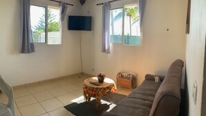 A living room with a sofa, a small table with a plant, and a TV mounted on the wall. - Holiday rental in Petit-Canal (Guadeloupe) (PETIT-CANAL)