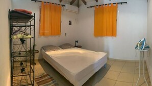 A bedroom with a bed, a metal shelf unit, and two orange curtains. - Holiday rental in Petit-Canal (Guadeloupe) (PETIT-CANAL)