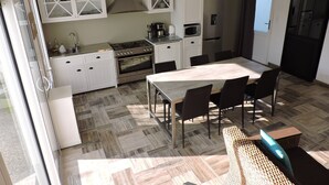 A compact kitchen with white cabinets, a stove, oven, microwave, and a dining area with a table and chairs. - Au Vieil, house with spa, sauna, bikes 200m from the beach and shops (Noirmoutier-En-L'île)