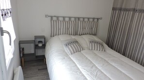 A neatly made bed with striped bedding, a bedside table with a lamp, and a window with curtains. - Au Vieil, house with spa, sauna, bikes 200m from the beach and shops (Noirmoutier-En-L'île)