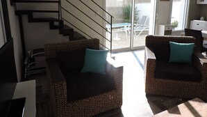 A modern living room with wicker furniture, a staircase, and a sliding glass door leading to an outdoor patio. - Au Vieil, house with spa, sauna, bikes 200m from the beach and shops (Noirmoutier-En-L'île)