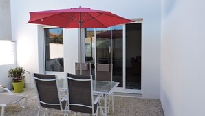 A patio with a table and chairs, a red umbrella, and a sliding glass door leading to an outdoor area. - Au Vieil, house with spa, sauna, bikes 200m from the beach and shops (Noirmoutier-En-L'île)