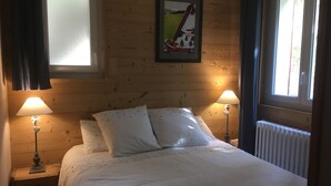 A bedroom with a bed, two bedside lamps, a poster on the wall, and a window with curtains.