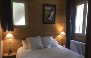 A bedroom with a bed, two bedside lamps, a poster on the wall, and a window with curtains.