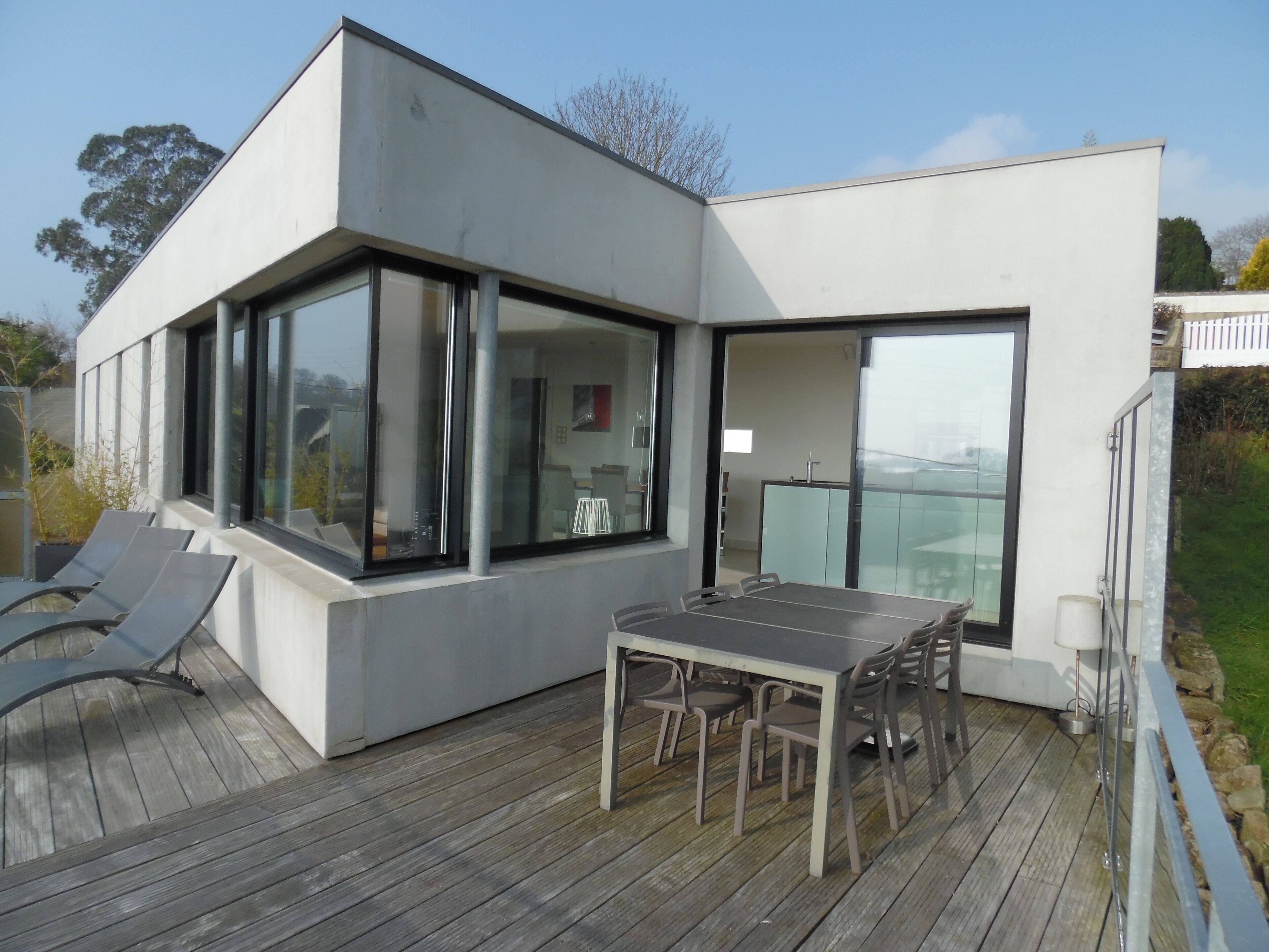 A modern house with a deck, large windows, and a dining area.