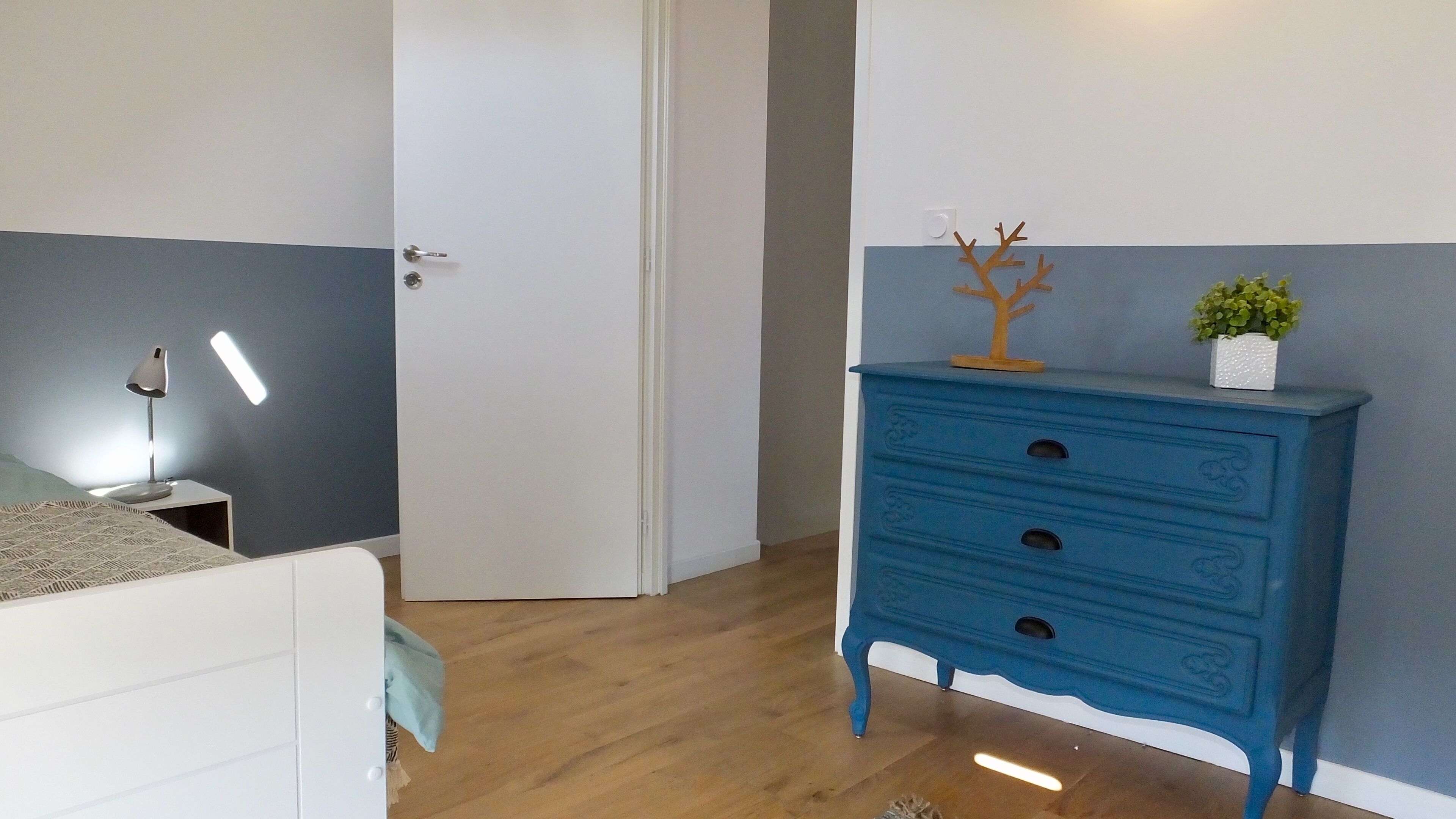 Une chambre à coucher avec un lit, une table de chevet, une lampe, une commode et une porte.