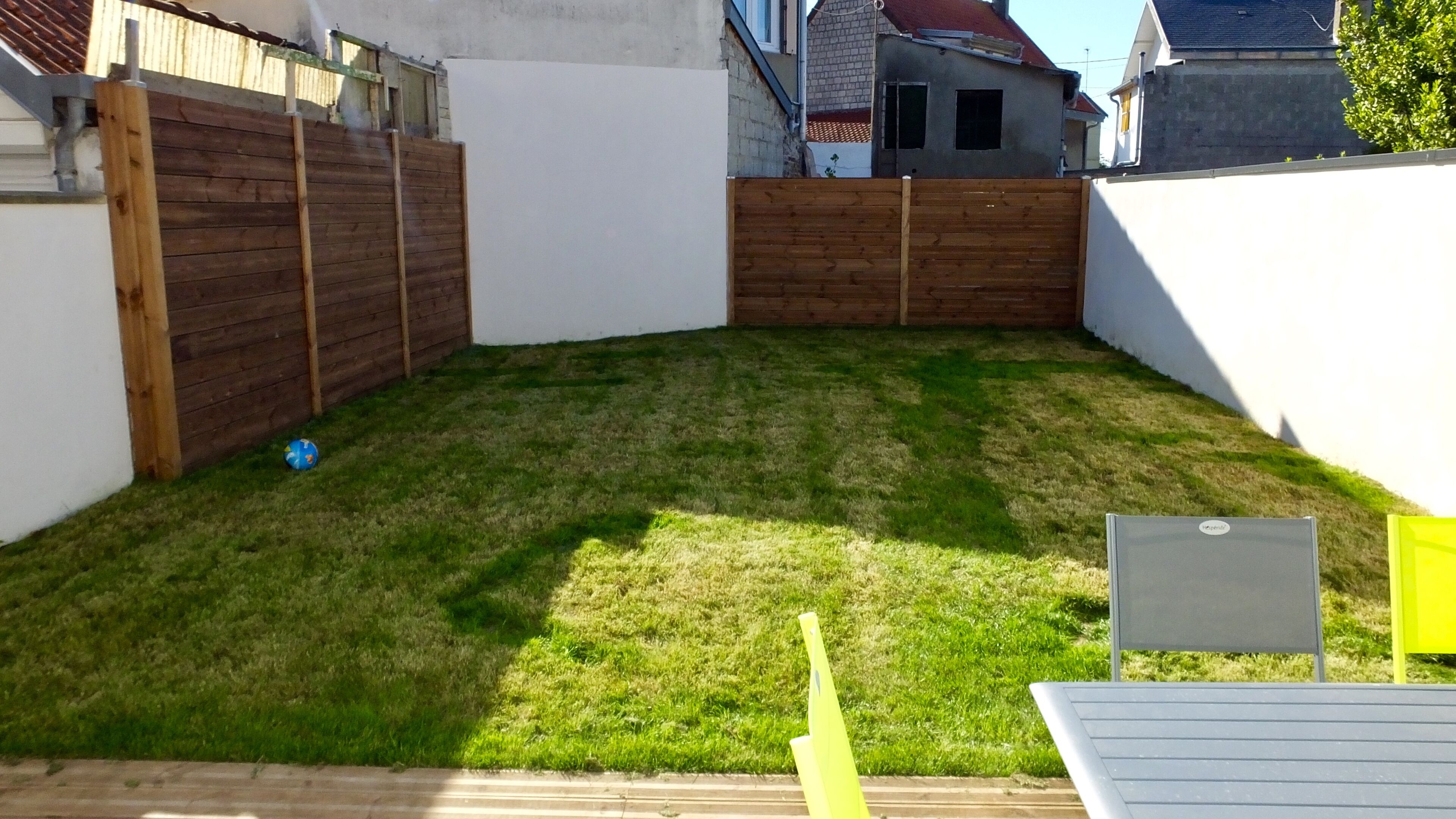 Un patio trasero con valla de madera, césped y pared blanca.