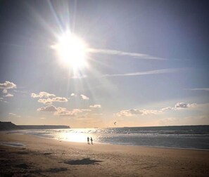 Una playa con cielo despejado, sol y algunas personas caminando.