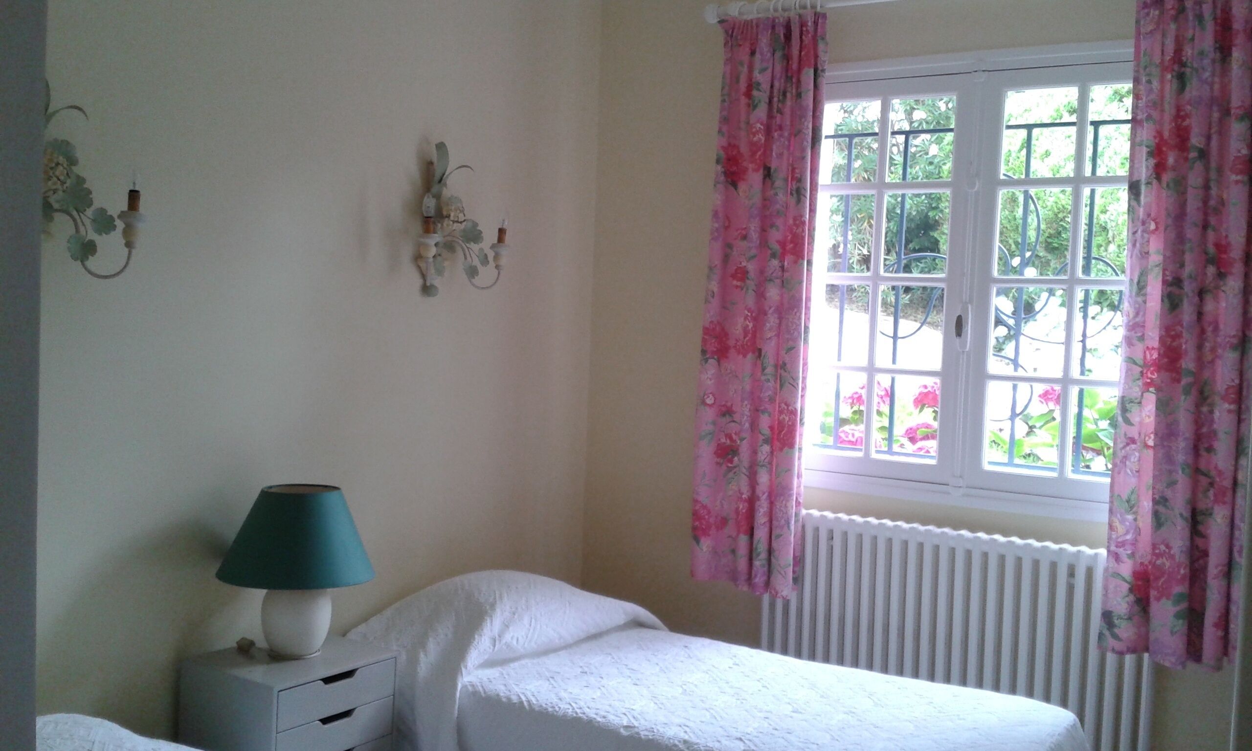 A bedroom with a window, a bedside table with a lamp, and a radiator.