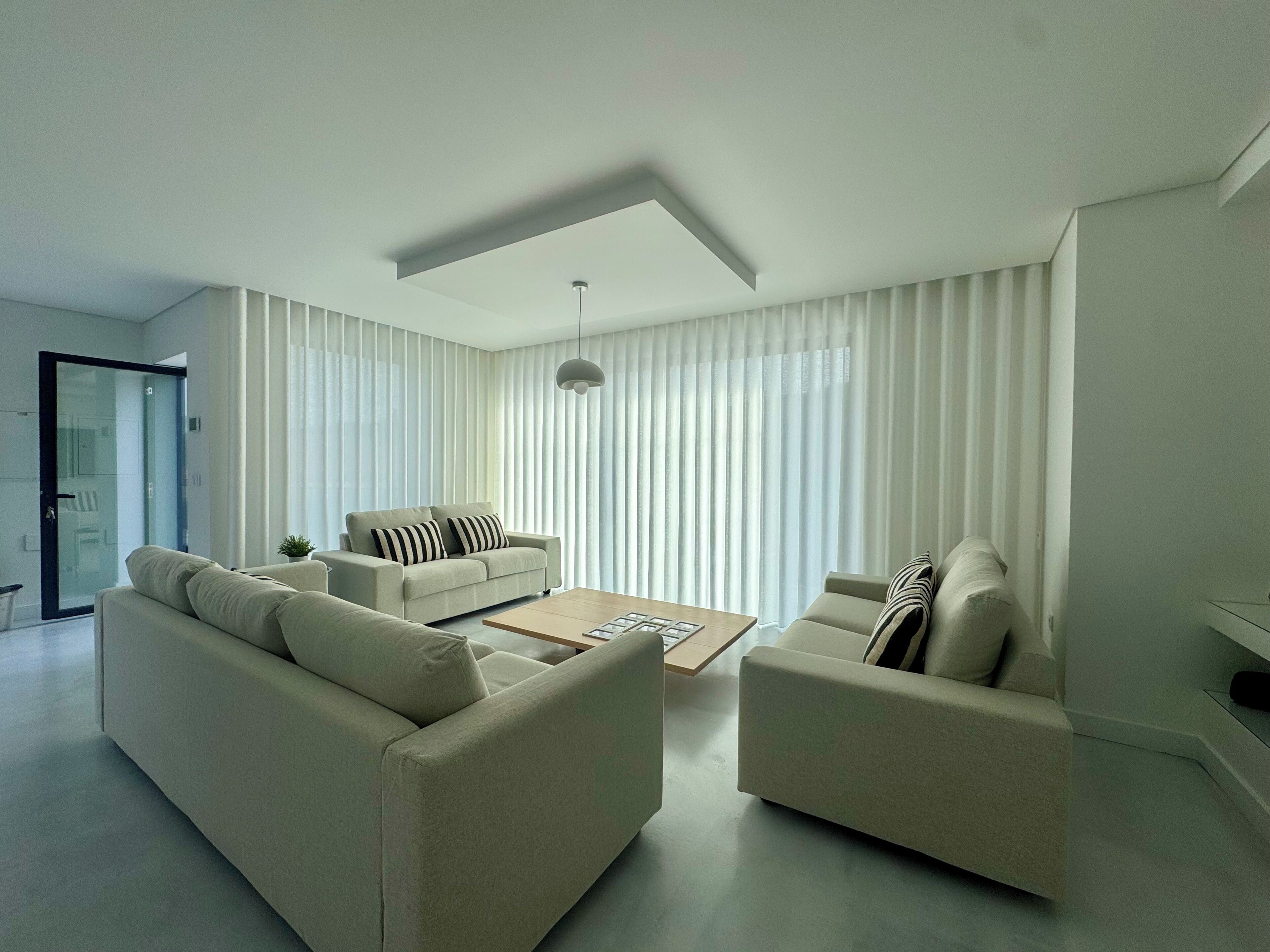 Een moderne woonkamer met een bank, fauteuils, een salontafel en een hanglamp.