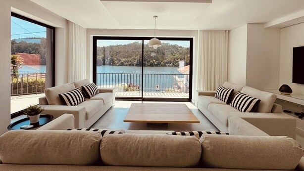Un salon moderne comprenant un ensemble de canapés, une table basse et une grande porte-fenêtre coulissante donnant sur un balcon avec vue sur le lac.