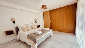 Une chambre moderne avec un grand lit, une armoire en bois et un luminaire suspendu.