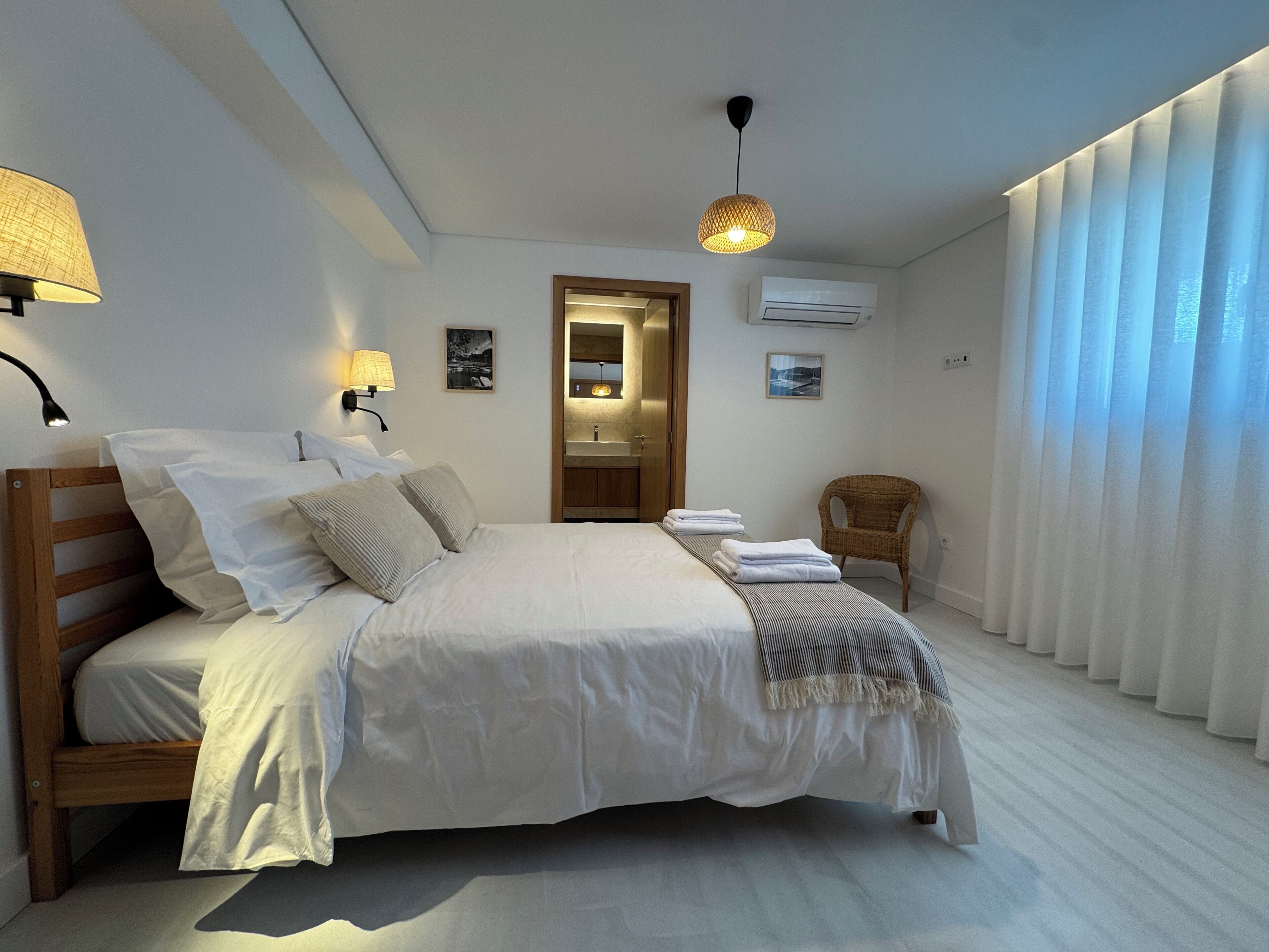 Une chambre à coucher comprenant un lit, des lampes de chevet, une chaise, un miroir et une porte donnant sur une salle de bain.