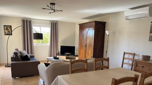 Une pièce bien éclairée, avec un canapé, une table à manger et des chaises, un téléviseur, un meuble et une lampe sur pied.