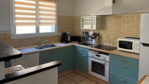 Une cuisine avec des meubles de couleur turquoise, un évier, une cuisinière, un four à micro-ondes et une fenêtre avec des stores.