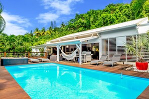 A swimming pool with lounge chairs and a barbecue area, surrounded by lush greenery.