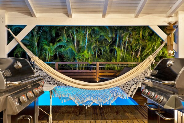 A hammock under a wooden ceiling with a view of a tropical forest.