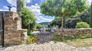 A rustic outdoor seating area with stone flooring and a stone wall, surrounded by greenery and a view of hills. - Cottage, quiet - On the heights of Anduze - 4 people (Anduze)