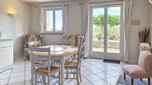 A dining area with a round table and chairs, a window with curtains, and a view of greenery outside. - Cottage, quiet - On the heights of Anduze - 4 people (Anduze)