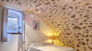 A bedroom with a sloped ceiling, a bed, a bedside lamp, a small table, and a window with curtains. - Cottage, quiet - On the heights of Anduze - 4 people (Anduze)