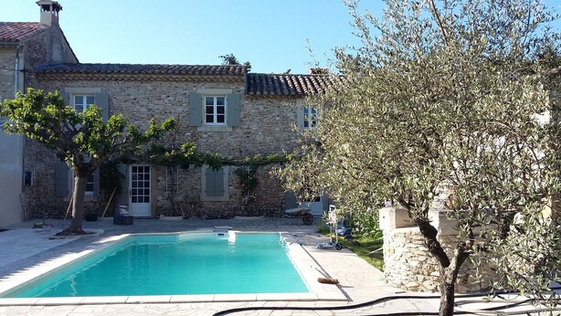 Un bâtiment en pierre avec une piscine, un arbre et un ciel bleu dégagé.