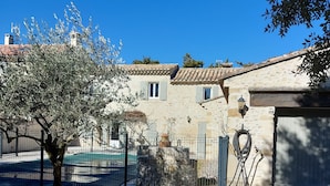 Un bâtiment rustique en pierre, avec un toit en tuiles, une cour clôturée et un arbre.