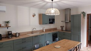 Une cuisine moderne avec une table à manger en bois, des meubles de rangement verts et un luminaire suspendu.