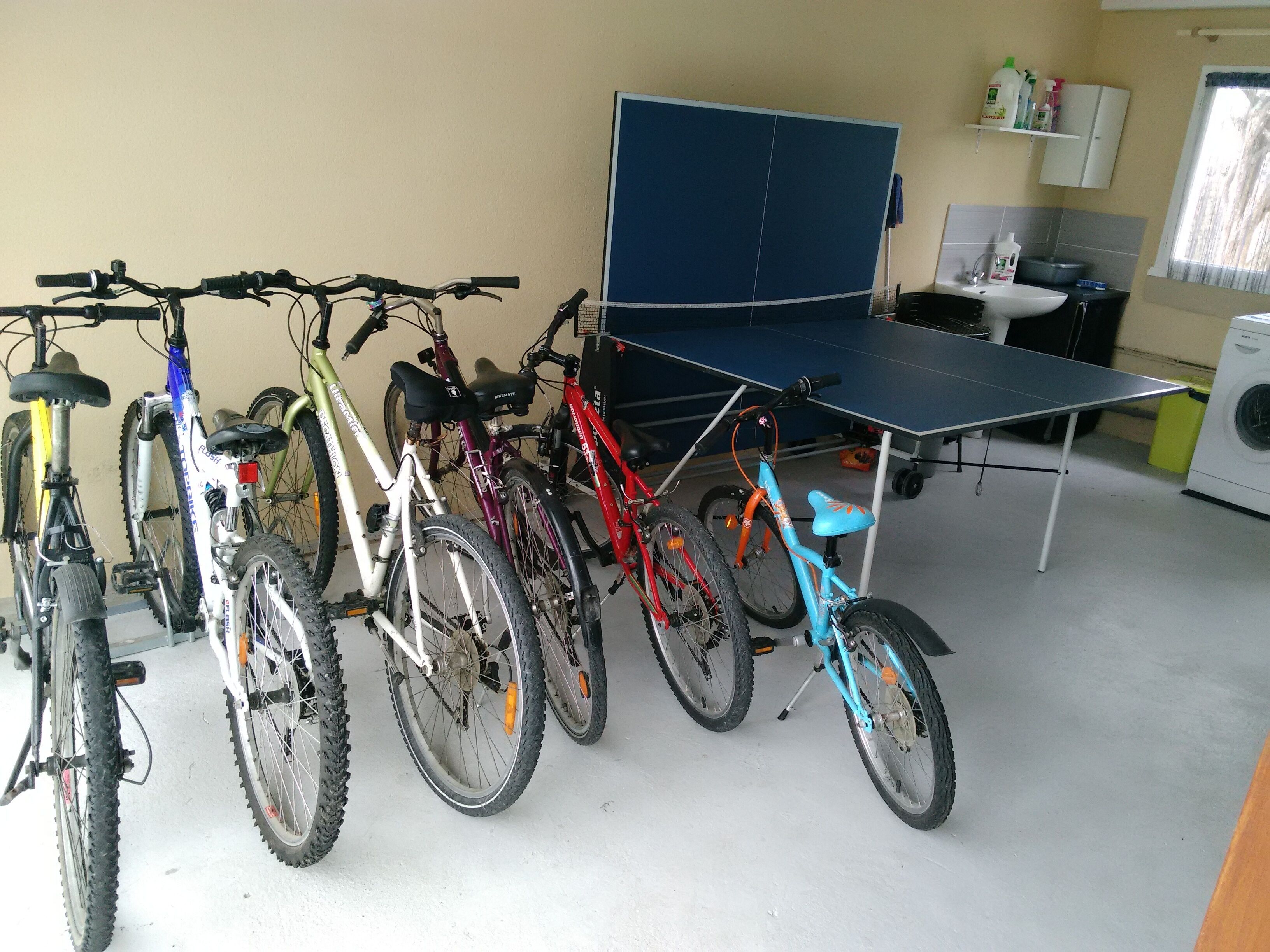 Des vélos sont garés dans une pièce où se trouvent une table de ping-pong et un lave-linge.