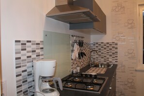 Une cuisine équipée d’une cuisinière à gaz, d’une machine à café et d’un plan de travail carrelé.