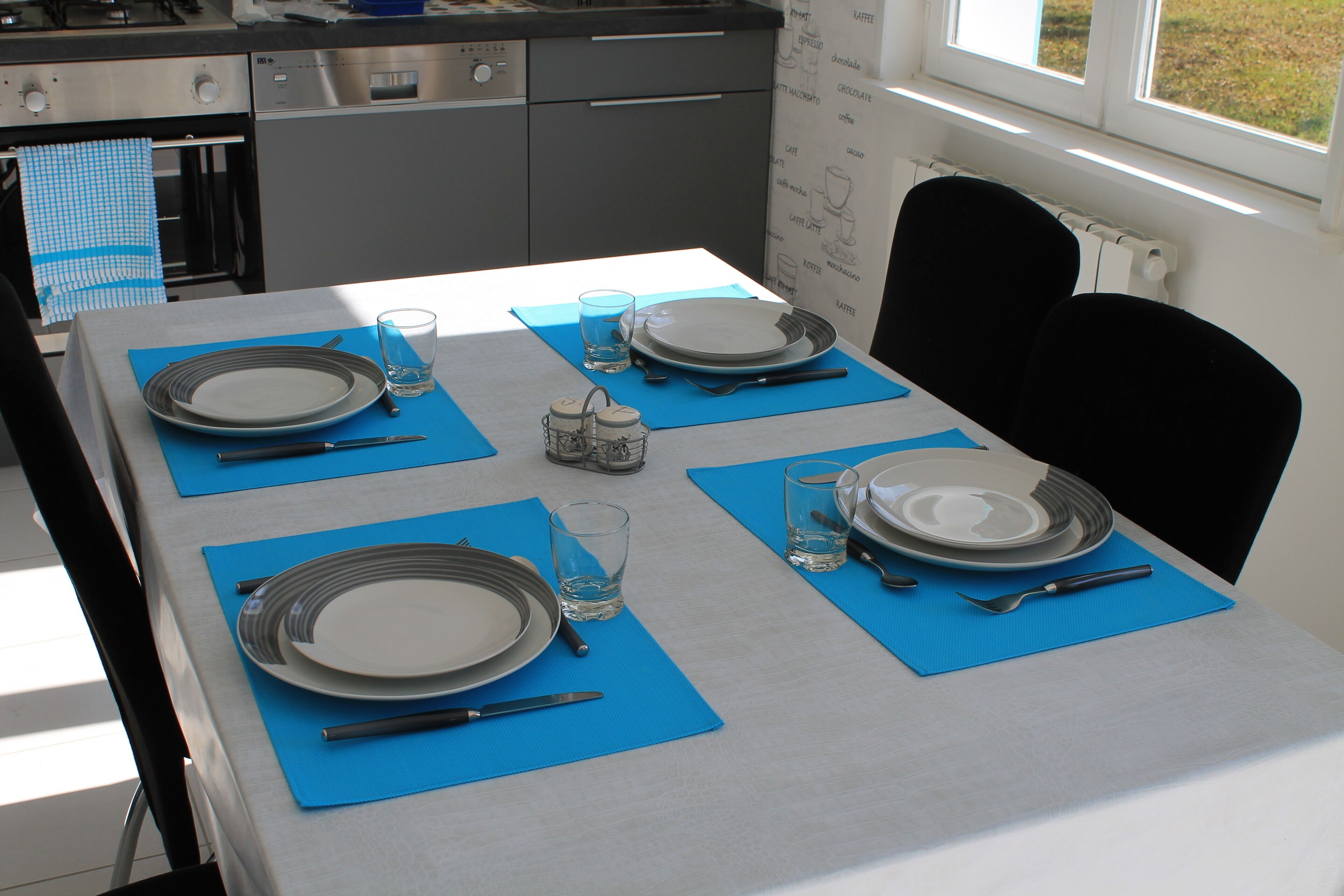 Une table à manger élégamment dressée, avec des sets de table bleus, des assiettes, des verres et des couverts.