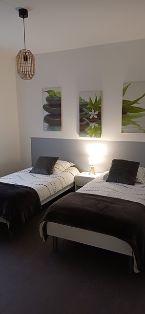 A bedroom with two beds, a bedside table with a lamp, and wall art.