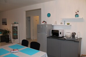 Une cuisine compacte équipée d’un réfrigérateur, d’un four à micro-ondes et d’un petit plan de travail avec un évier. On y trouve une table à manger avec des sets de table bleus et un livre posé dessus.