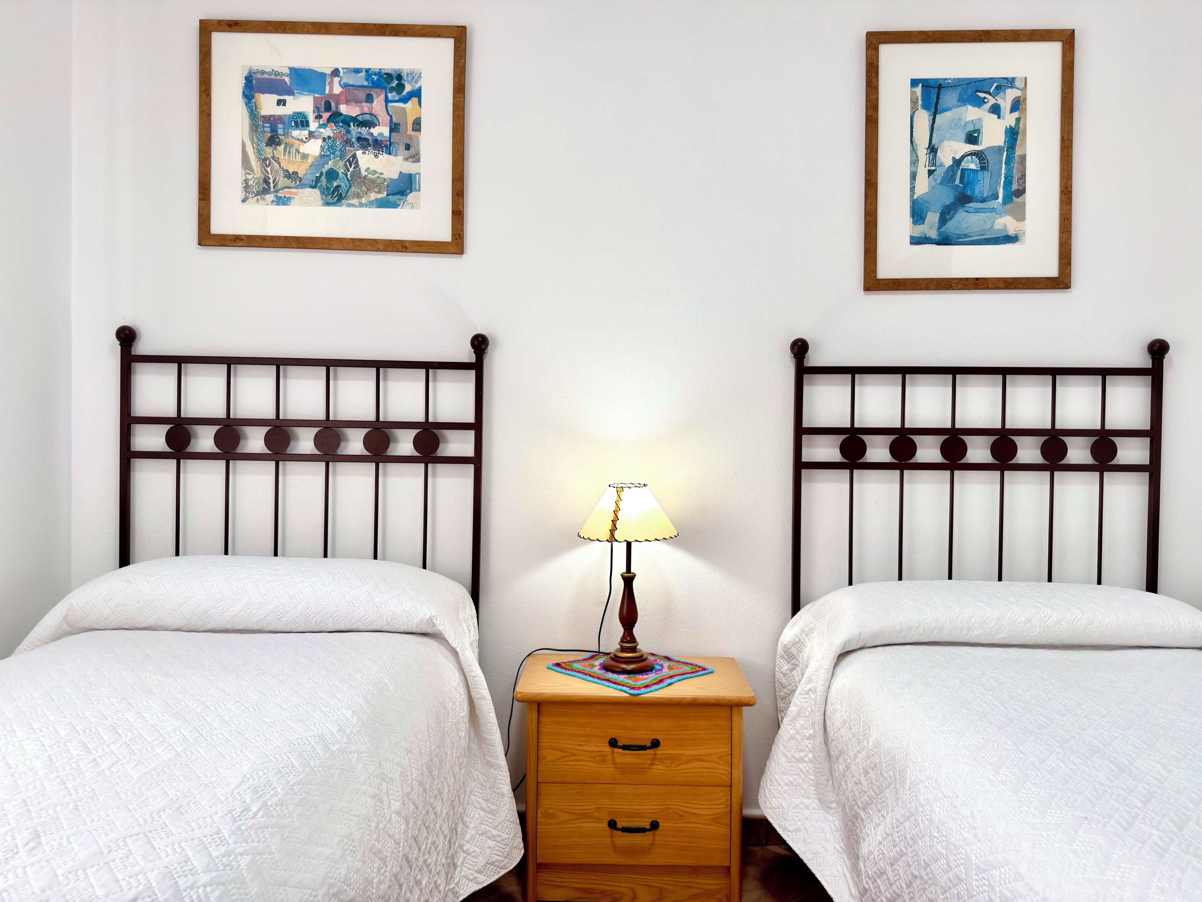 A room with two beds, a nightstand, and two framed artworks on the wall.