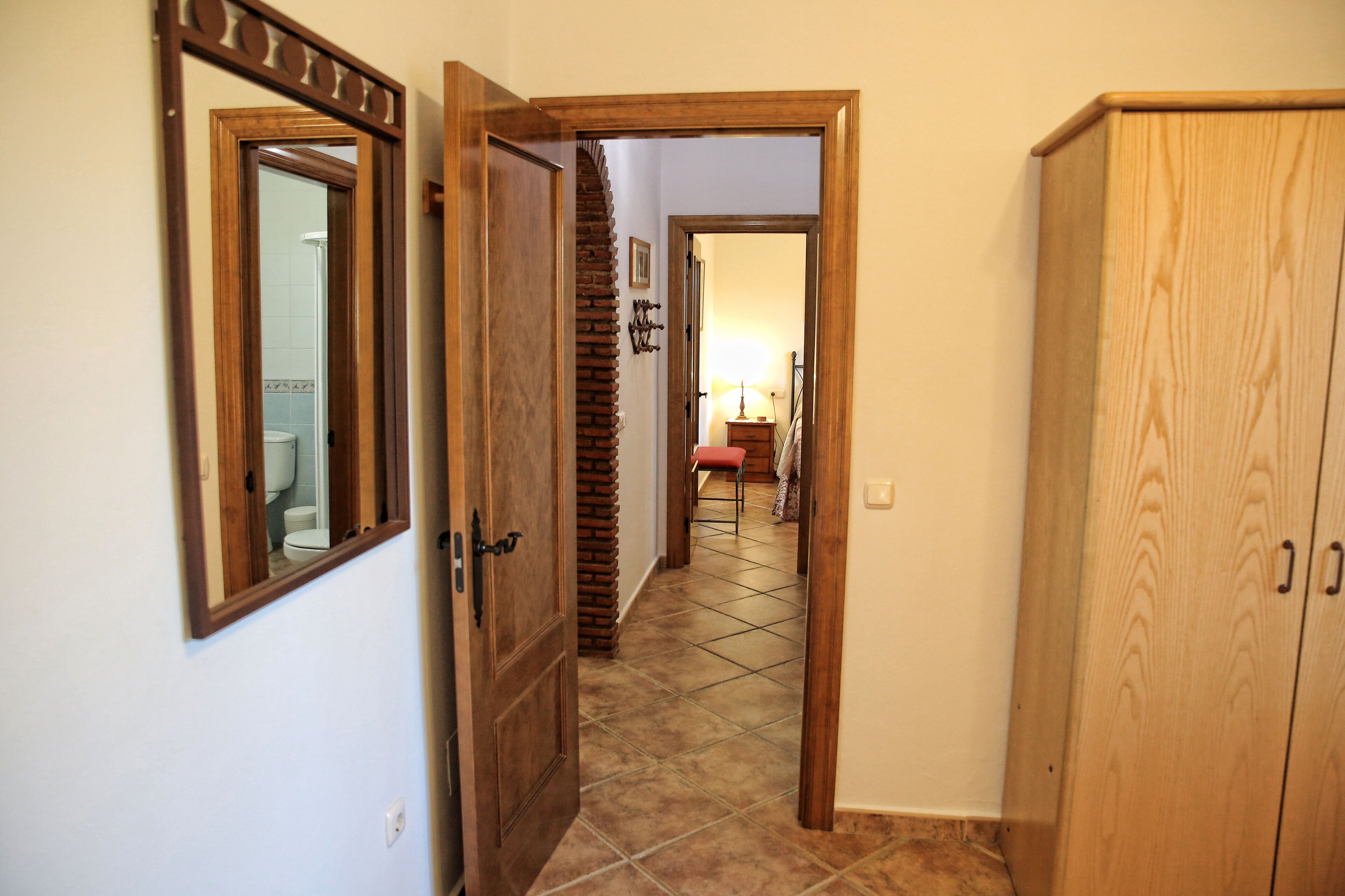 A hallway with a wooden door, a tiled floor, and a wooden cabinet.