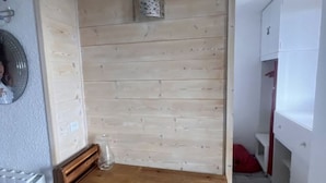 Un pequeño escritorio de madera con un florero de vidrio, un radiador blanco y un armario blanco en una habitación con paneles de madera.